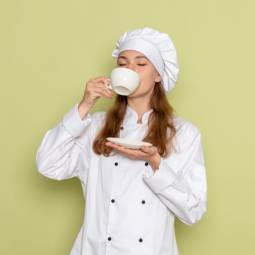 front-view-female-cook-white-cook-suit-drinking-coffee-green-wall-min